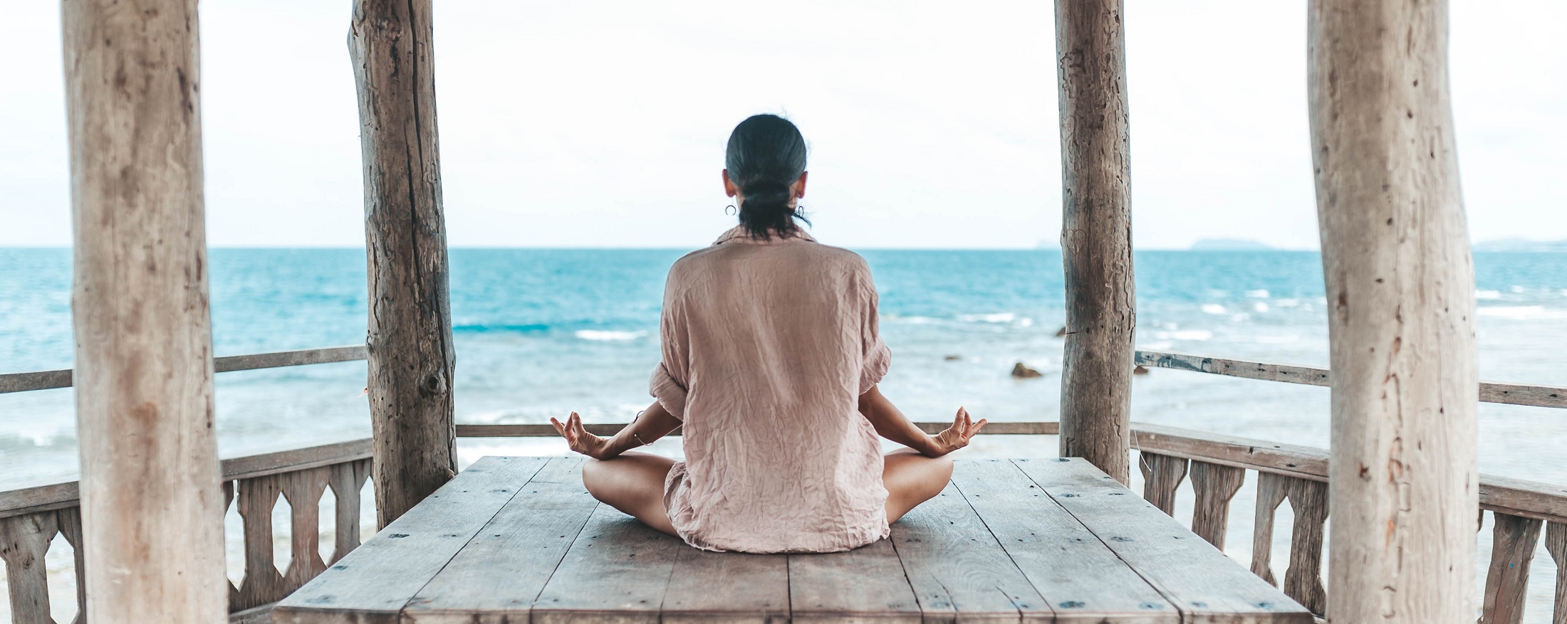 young woman meditating in a yoga pose in a gazebo at the beach